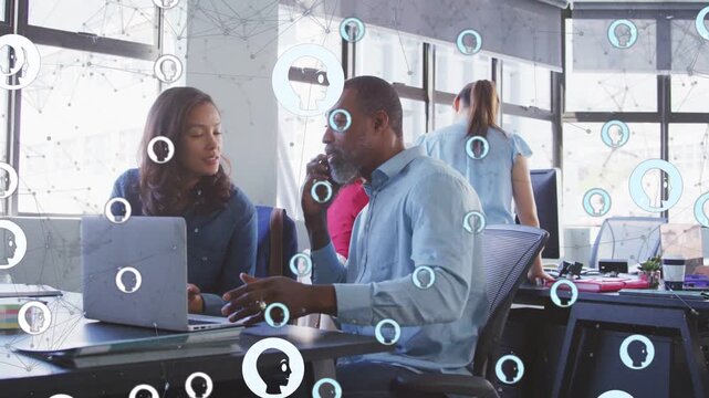 Man taking call pointing at laptop, peer working business update, animated icons drifting over desk