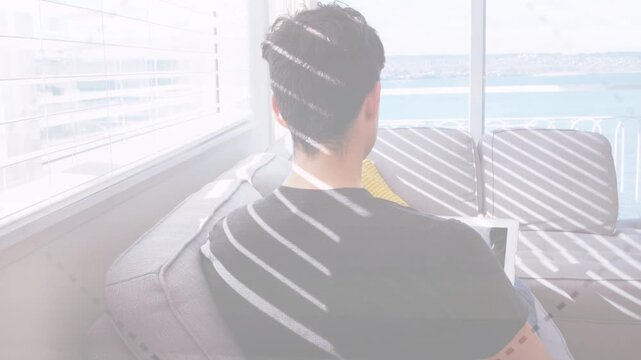 Man on sofa facing balcony, sunlight shifting through blinds causing tech work posture shifts