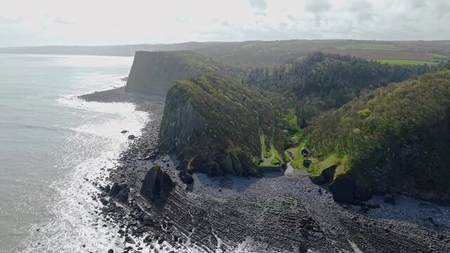 Aerial view of Mouthmill Beach which is a secluded pebble cove near Clovelly, North Devon, known for the dramatic Blackchurch Rock sea arch and waterfall. Ambient exploration by drone. 