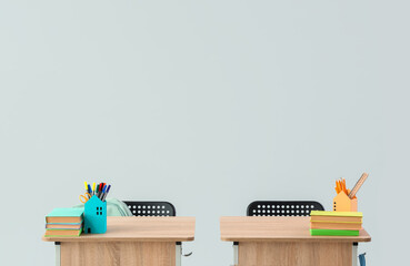 Modern school desks with books and stationery on grey background