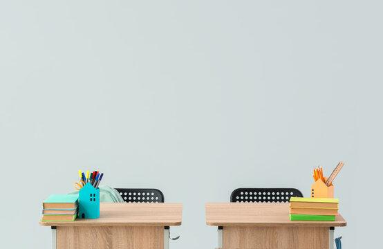 Modern school desks with books and stationery on grey background