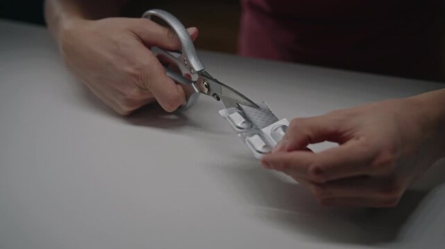 Hands using scissors to cut blister pack to split pills for precise dosing, concept of personal medication management, daily regimen adherence, and healthcare routine, close-up, slow motion.