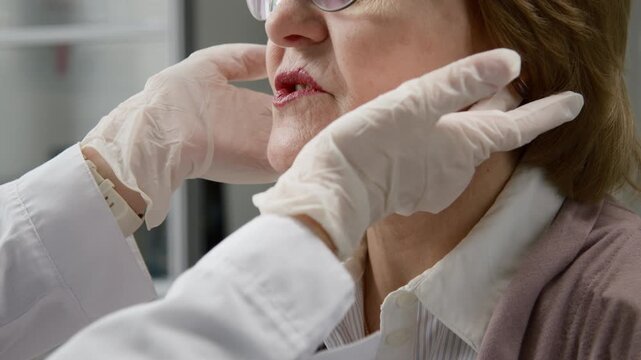 Cropped close up shot of unrecognizable elderly woman receiving physical examination at clinic while gloved hands of doctor checking lymph nodes for swelling