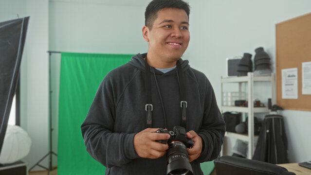 Man photographer holds camera and checks settings while smiling in studio with green backdrop and softbox; contentment creativity craft.