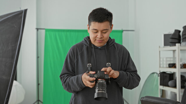 Man photographer holding dslr camera, fingers adjusting lens and checking settings in studio; concentration craft.