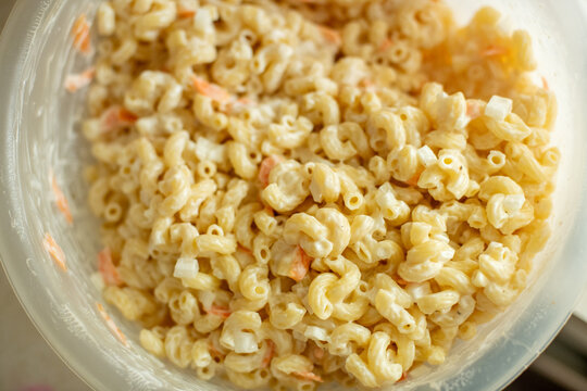 A plastic dish of macaroni salad made with cavatappi pasta, mayonnaise, and sliced carrots, a classic summer barbecue and Memorial Day side dish.