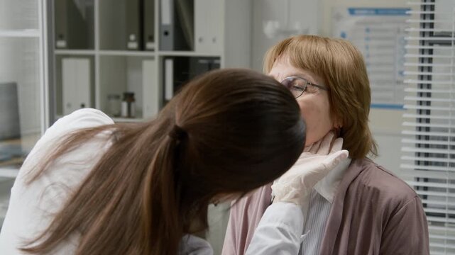 Medium shot of senior woman with glasses undergoing lymph nodes examination by young adult female doctor during cancer monitoring at modern clinic