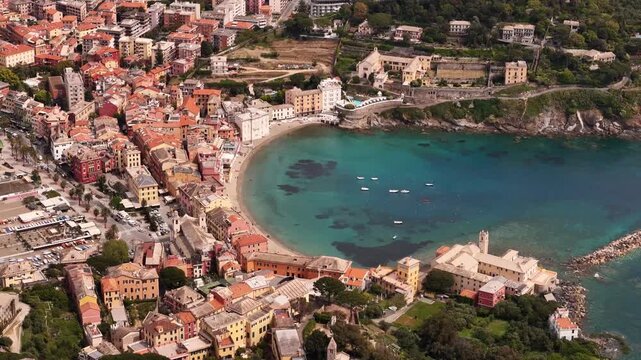Aerial view of the Bay of Silence with its sandy beach, turquoise water, and colorful historic buildings along the coastline in Sestri Levante, Liguria, Italy.