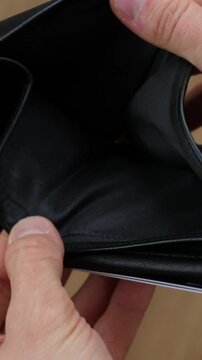 Caucasian male hands opening an empty black leather wallet, revealing no money inside, illustrating concepts of poverty, debt, bankruptcy, unemployment, and financial crisis or recession