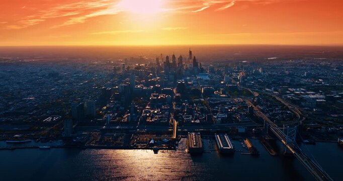 Setting sun in the orange sky lights the cityscape of the modern city. Aerial perspective on the stunning scenery of Philadelphia, Pennsylvania, USA at golden hour.