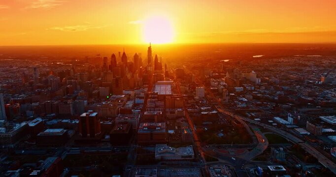 Flight over the cityscape lit by the bright orange setting sun. Approaching the skyscraper downtown of Philadelphia, Pennsylvania, USA from drone.