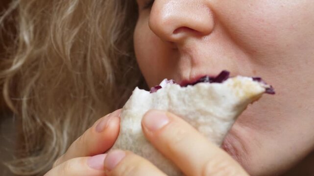 Close up video of a young woman with curly hair hungrily eating a tasty vegetarian burrito wrap, showing the satisfaction of enjoying a quick and delicious street food meal for lunch