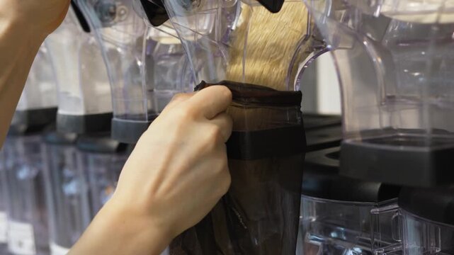 Woman's hands filling a reusable mesh produce bag with quinoa from a gravity bin dispenser in a sustainable, plastic free grocery store, promoting an eco friendly and healthy lifestyle