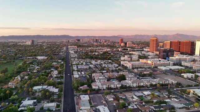 Aerial view of North 7th Street stretching toward the downtown skyline with office buildings and distant mountains under a soft sunset sky in Phoenix, Arizona, United States.