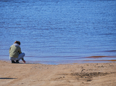Woman Alone at Water's Edge Touching Sand &mdash; Solitude Contemplation Mindfulness Nature Connection Lake Shore Concept
