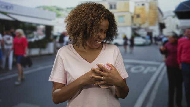 Woman holding heart shaped gift box to chest on busy city street smiling with closed eyes; joy gratitude.