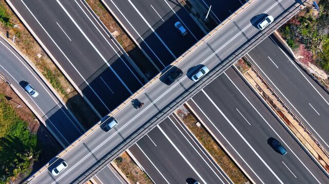 Top down aerial view of highway overpass bridge. Overhead drone shot showing vehicles driving on a multi-lane asphalt highway and a concrete bridge.