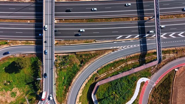 Complex highway interchange and overpass aerial view. Detailed top-down drone shot of multi-level roads, pedestrian bridge, and cycle path in Spain.