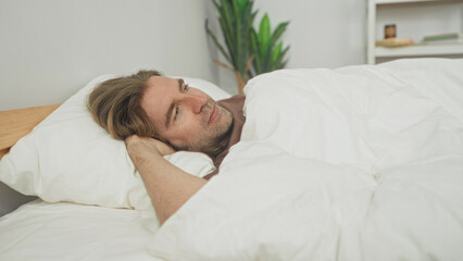 Man lying in bed with hand behind head on pillow under white duvet cover, bedroom  serenity contemplation. © Krakenimages.com