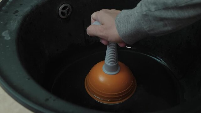 Home plumber repairing sink drain. Closeup of hand operating sink plunger. Practicing DIY plumbing repair. Repetitive suction action with rubber cup to unclog drain efficiently