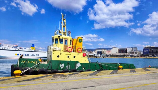 Photo of the tugboat Ektoras (Hector) docked in the inner Port of Piraeus, Greece, with an ANEK Lines ferry and Akti Kondyli skyline in the background. 