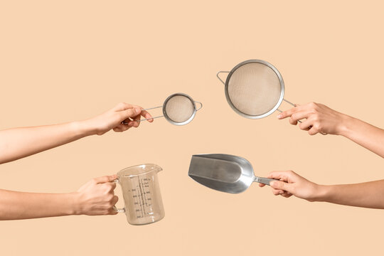 Female hands holding sieves with measuring cup and scoop on beige background