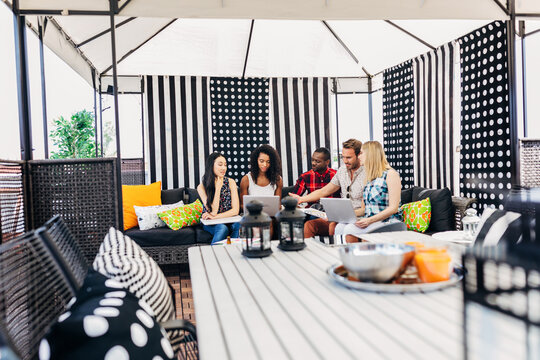 Group of friends collaborating on laptops in patio gazebo