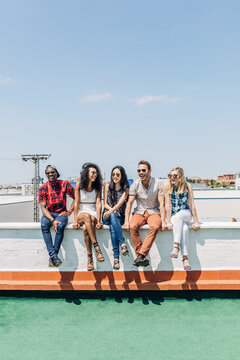Group of friends sitting on rooftop ledge in summer sun