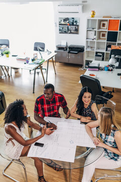 Team meeting around blueprints in modern design office