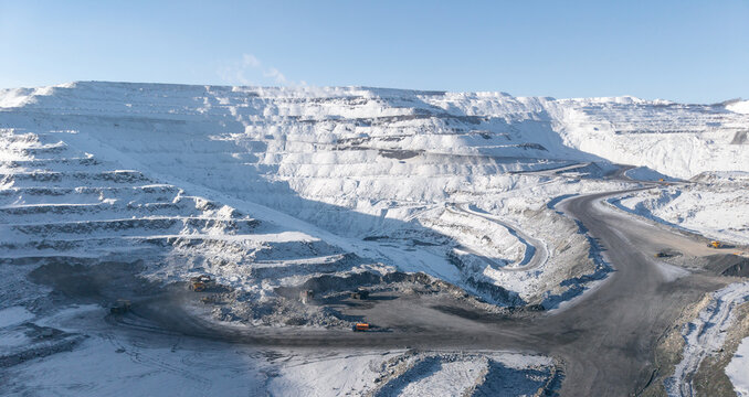 Winter landscape of open pit coal mine with snow-covered terraces and machinery