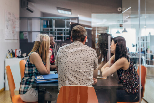 Diverse coworkers meeting in modern office behind glass wall