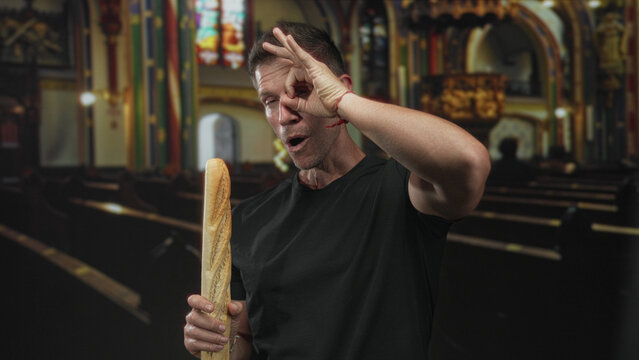 Man smiling while holding a baguette and making ok hand gesture in church building; faith contrast playful.