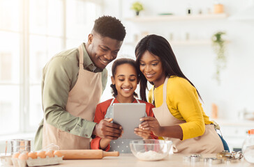 Fototapeta premium A family spends time cooking in the kitchen. They look at a tablet to check recipes. They share smiles and laughter while preparing food together. The kitchen is bright and welcoming.