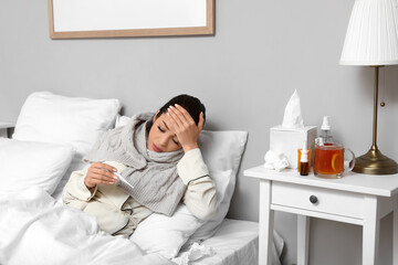 Fototapeta premium Ill young woman with thermometer lying in bedroom