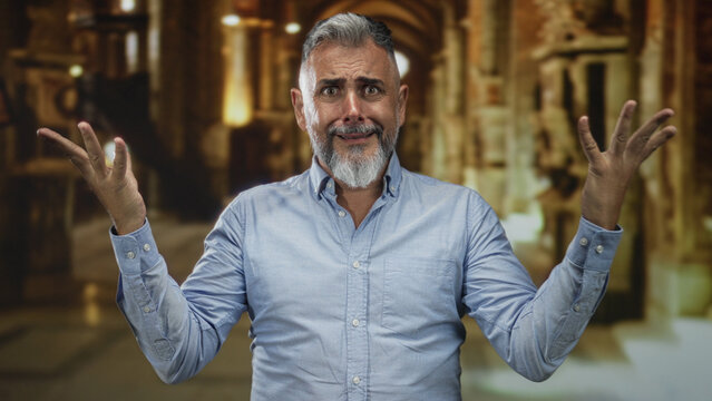 Middle aged man with raised bare hands looking upward toward a vaulted ceiling inside a church building, open collar visible; pleading faith doubt.