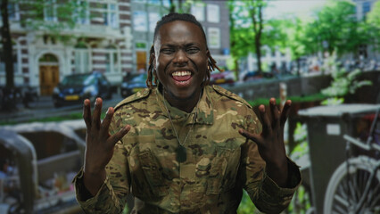 Obraz premium Man in camouflage military jacket holds hands on head on amsterdam canal street beside water and bicycle, dogtags visible; stress duty.