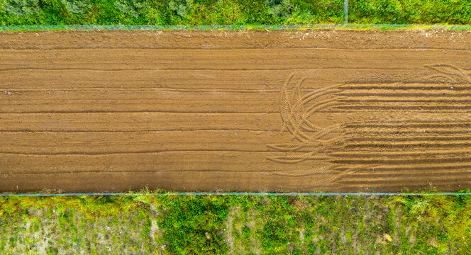 Direct overhead drone perspective sweeping across a bare brown agricultural plot characterized by striking horizontal plow lines ending with distinct curved tractor turn marks