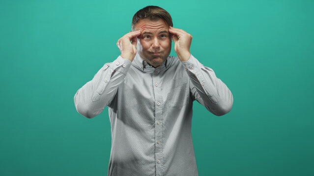 Man presses temples, puckers cheeks and gestures with raised hands in studio; frustration concentration.
