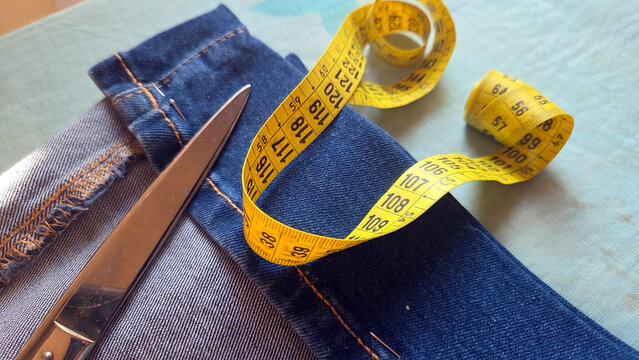 Closeup of denim jeans with scissors and coiled yellow measuring tape for tailoring background and clothing repair design