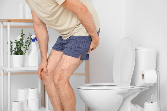 Man sitting down on toilet bowl in restroom. Hemorrhoids concept
