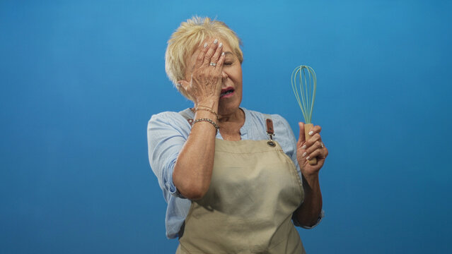 Woman cook in studio holds whisk and covers face with hand, apron visible and closed eyes, short hair; frustration perseverance.