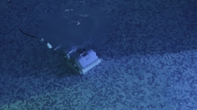 Robotic pool cleaner reversing and turning on mosaic tile floor underwater while cleaning swimming pool with blue light. High quality 4k footage