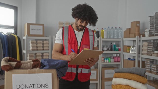 Man sorting donated clothing into a labeled donations box in a charity building while writing on a clipboard; community service compassion.