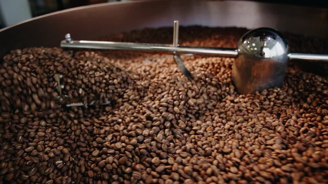 Slow motion roasted coffee beans tumbling and stirring inside industrial cooling drum at small batch roastery during post roast.