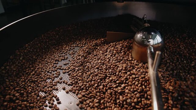 Closeup roasted coffee beans in industrial roaster background for banner and product packaging with detailed brown texture.