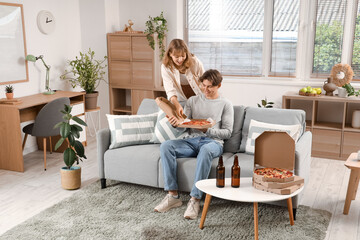 Obraz premium Beautiful young couple holding cardboard box with tasty pizza in living room