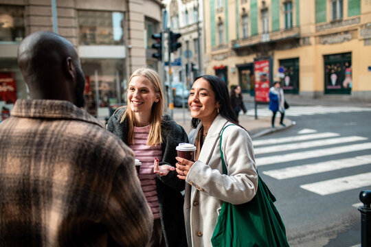 Three friends chatting over coffee at city crosswalk