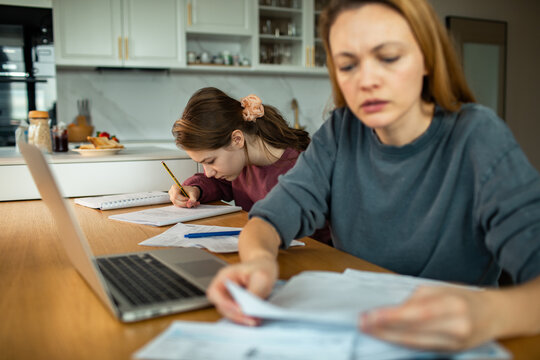 Parent managing bills while child does homework at the kitchen table