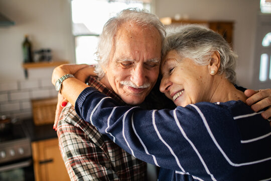 Smiling senior couple hugging at home kitchen