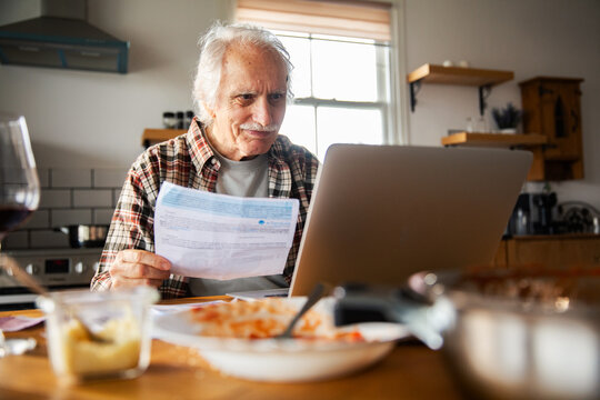 Senior man paying bills online at home kitchen